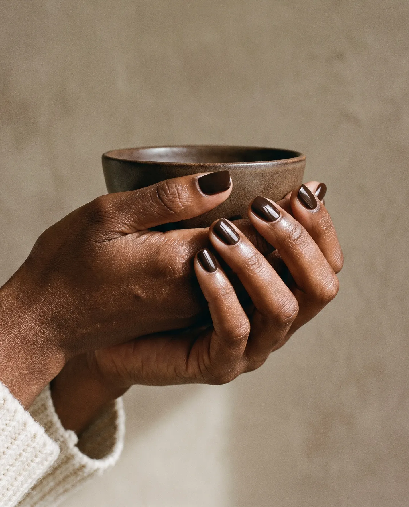 Hands with a glossy espresso-brown manicure cradling a stoneware cup